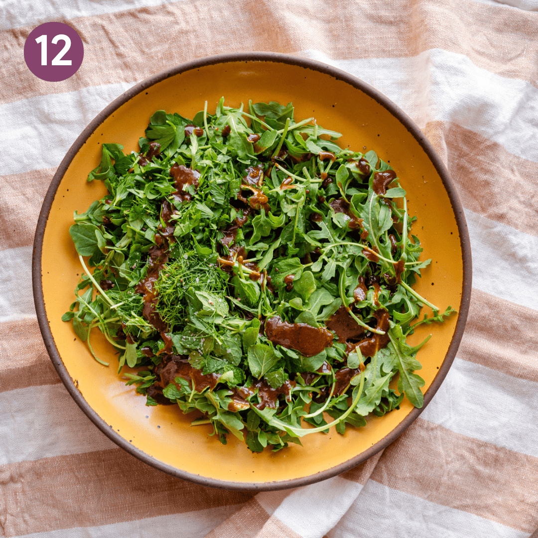 Balsamic vinaigrette added to bowl of greens. 